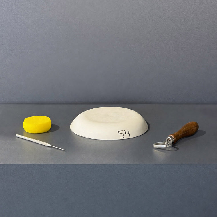 White pottery plaster hump mold number 54: a shallow oval dome, rim-down on the gray shelf.