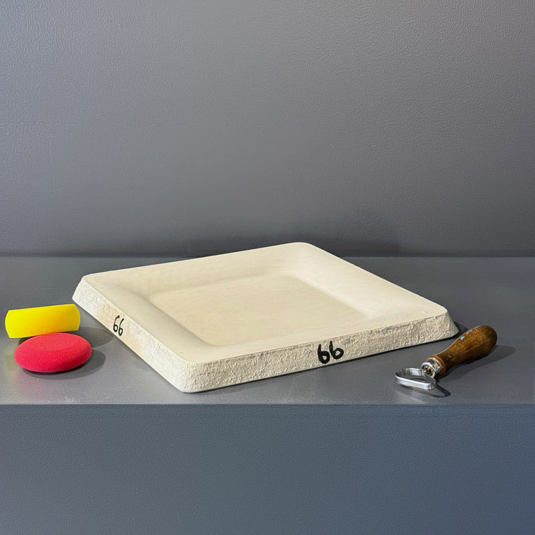 White plaster mold number 66: a shallow square tray mold, sitting at an angle on the gray shelf with a recessed square well.