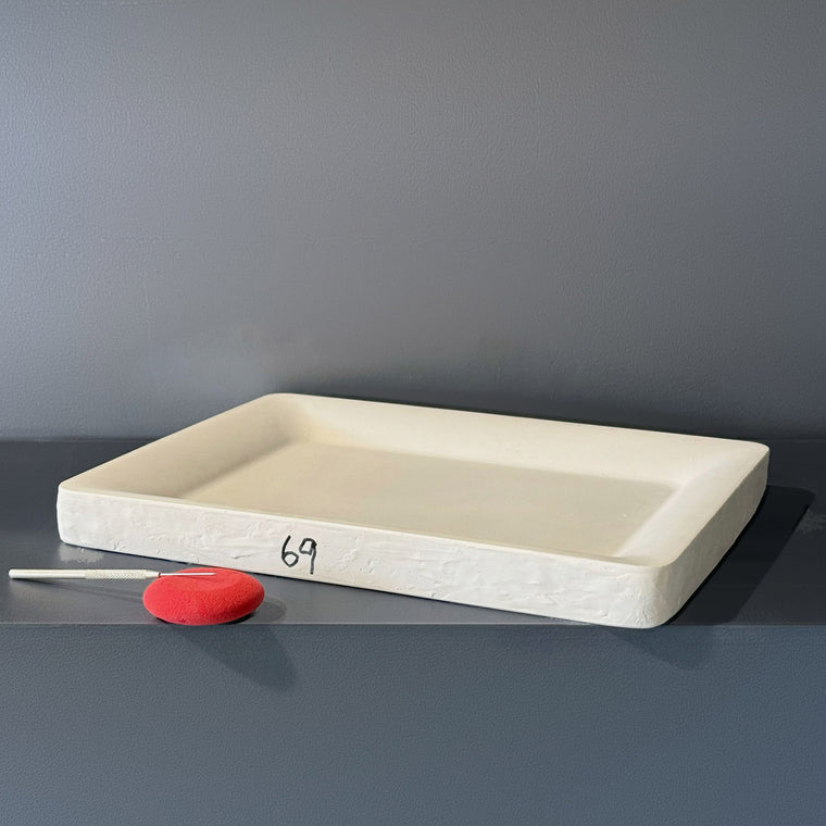 Large white plaster tray mold number 69: a rectangular tray, measuring 17 in wide, 12.88 in deep and 1.62 in tall with a broad flat floor and low walls, sitting cavity-up on the gray shelf.