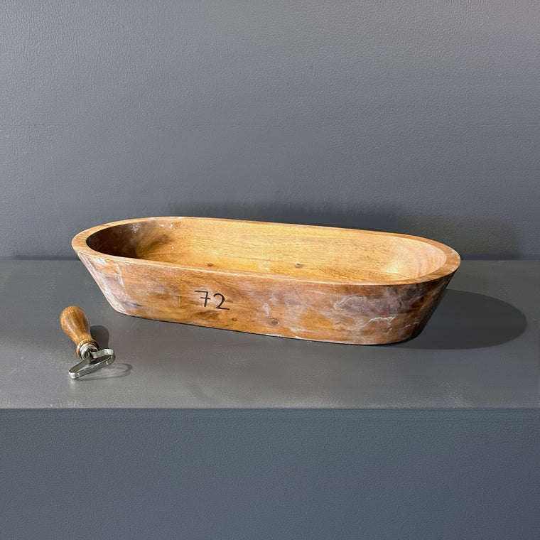 Elongated wooden dough bowl used as mold number 72, measuring 16.9 in wide, 8 in deep and 2.75 in tall with a hand-hewn surface, sitting upright on the gray shelf.