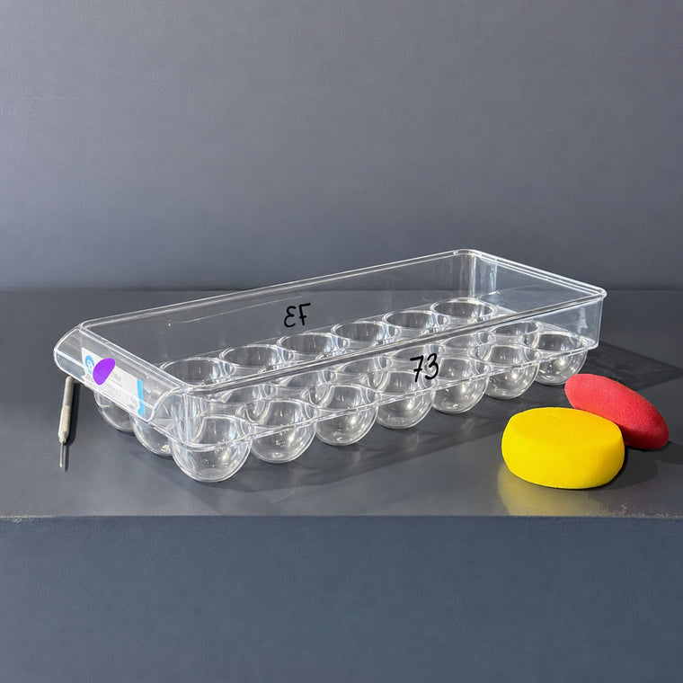 Clear plastic egg tray used as mold number 73: a rectangular tray, measuring 14.38 in wide, 6.3 in deep and 2.8 in tall with rows of rounded egg-shaped wells, sitting on the gray shelf.