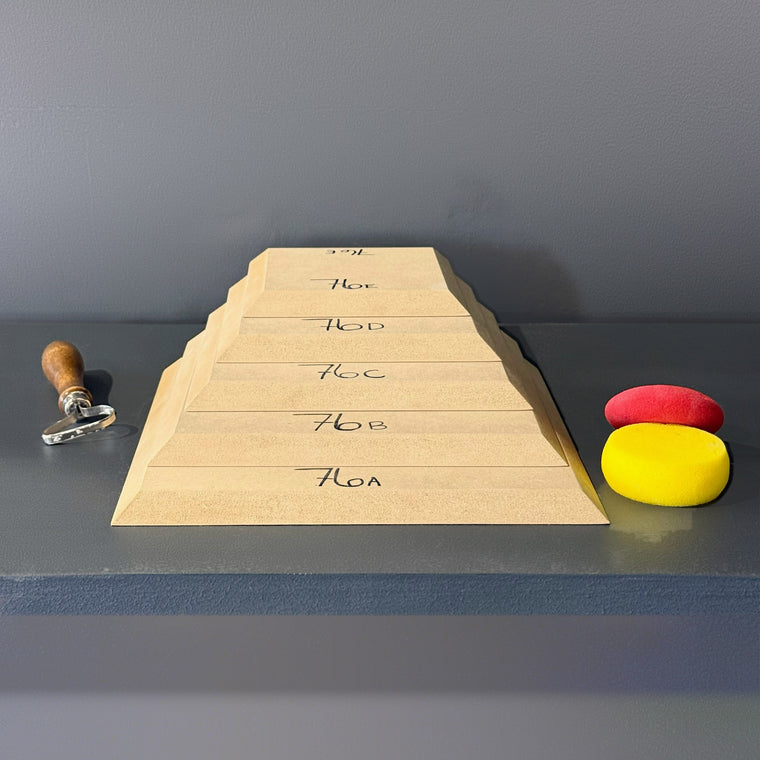 High-density fiberboard mold 76A: a rounded triangular board, the largest of a 5-piece nesting set shown stacked largest to smallest on the gray shelf, hand-labeled 76A.