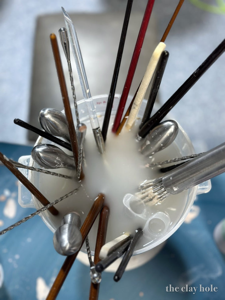 Pottery trimming tools and brushes soaking in a cup of murky clay water