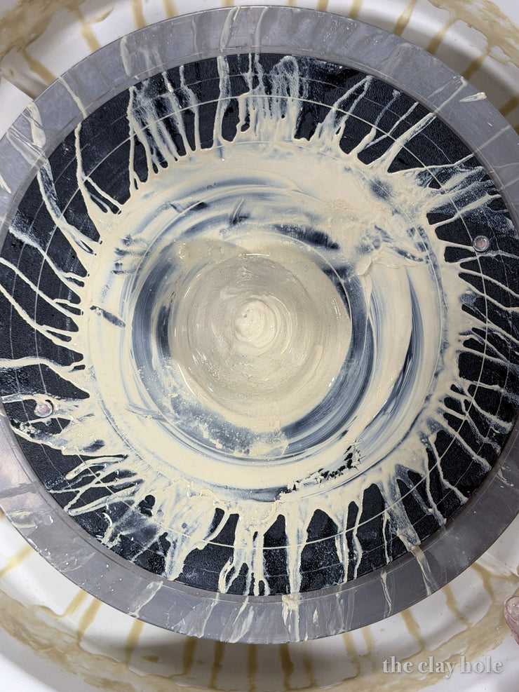 Clay slip flung outward in a radial sunburst pattern across a pottery wheel splash pan