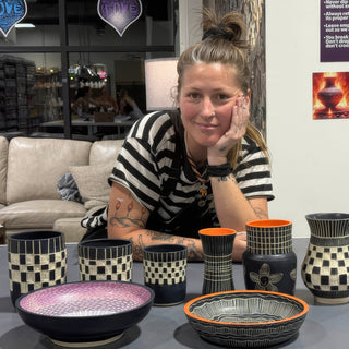A member resting chin on hand behind black and cream checkered vases, cups and carved bowls with orange accents at The Clay Hole pottery studio in Draper, Utah