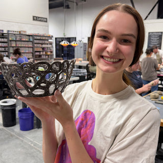A member holding a shallow black glossy bowl with a woven cutout pattern of looping lines at The Clay Hole pottery studio in Draper, Utah