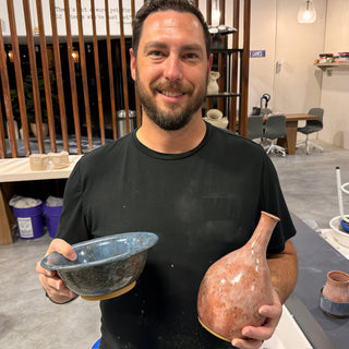 A member holding a blue glazed bowl and a pink and cream bottle shaped vase at The Clay Hole pottery studio in Draper, Utah
