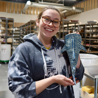 A member holding a blue shark-shaped piece with white dot patterns, side fins and a long tail at The Clay Hole pottery studio in Draper, Utah
