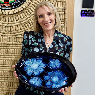 A member holding a glossy dark blue oval platter with four light blue flower shapes at The Clay Hole pottery studio in Draper, Utah