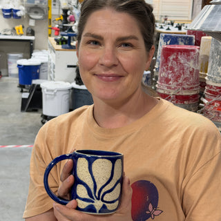A member holding a dark blue mug with a speckled cream flower design and a looped handle at The Clay Hole pottery studio in Draper, Utah