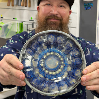 A member holding a round plate with deep blue glaze in a flower petal pattern around small bumps at The Clay Hole pottery studio in Draper, Utah