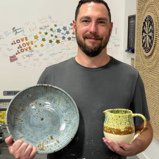 A member holding a wide pale blue bowl with brown flecks and a small yellow green speckled pitcher at The Clay Hole pottery studio in Draper, Utah