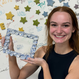 A member holding up a rectangular frame made of small round pieces with blue and white speckled glaze at The Clay Hole pottery studio in Draper, Utah