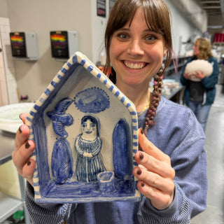 A member holding a house shaped blue and white dish with a striped rim and a raised figure inside at The Clay Hole pottery studio in Draper, Utah