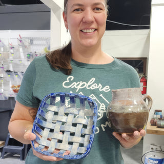 A member holding a square blue basket weave dish and a small brown glazed pitcher at The Clay Hole pottery studio in Draper, Utah