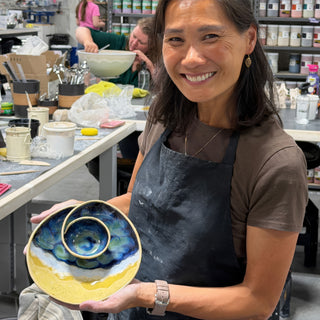 A member holding a round dish with a small bowl in the center and blue, white and yellow glaze at The Clay Hole pottery studio in Draper, Utah