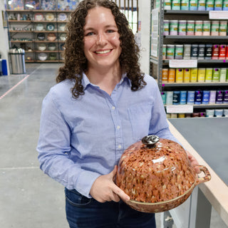 A member holding a domed lidded dish in glossy brown and tan speckled glaze with a side handle at The Clay Hole pottery studio in Draper, Utah