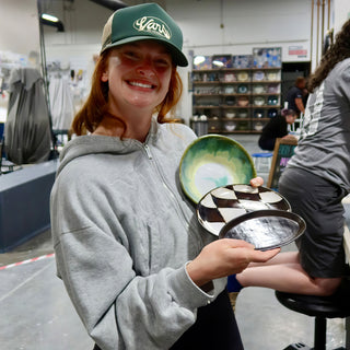 A member holding a green and cream bowl, a black and white checkered plate and a dark glossy plate at The Clay Hole pottery studio in Draper, Utah