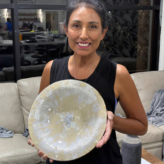 A member holding a large round shallow bowl with a mottled cream, white and pale blue glaze at The Clay Hole pottery studio in Draper, Utah