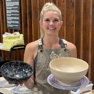 A member holding a small dark bowl with white speckles beside a large unglazed cream bowl at The Clay Hole pottery studio in Draper, Utah