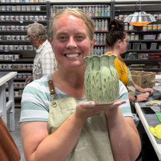 A member holding a small pale green vase with a ruffled rim and carved leafy stems on its sides at The Clay Hole pottery studio in Draper, Utah