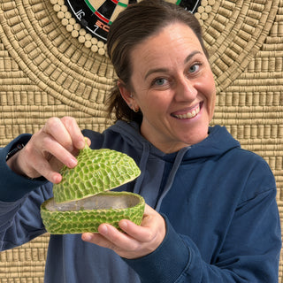 A member lifting the domed lid off a bright green dish covered in carved scale like texture at The Clay Hole pottery studio in Draper, Utah