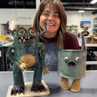 A member behind two creature sculptures, a tall teal monster with horns and a short gray blue one at The Clay Hole pottery studio in Draper, Utah