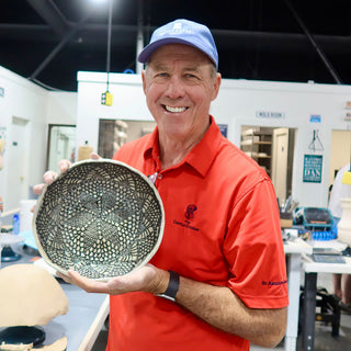 A member holding a wide shallow bowl with a dark lace-like pattern inside and a wavy pale rim at The Clay Hole pottery studio in Draper, Utah