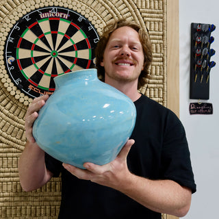 A member holding a large round glossy turquoise vase with a wide body and a short opening at The Clay Hole pottery studio in Draper, Utah