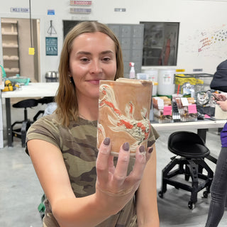 A member holding up a small rectangular vase with swirling red, orange and cream marbled color at The Clay Hole pottery studio in Draper, Utah