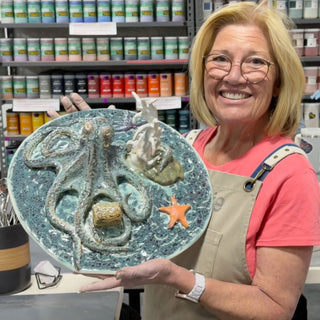 A member holding a large oval platter with a raised octopus, an orange starfish and white coral on blue-green glaze at The Clay Hole pottery studio in Draper, Utah