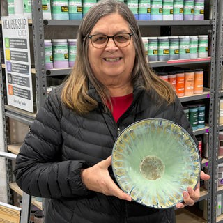 A member holding a wide shallow bowl in pale seafoam glaze with ribbed lines spreading out from a round center at The Clay Hole pottery studio in Draper, Utah