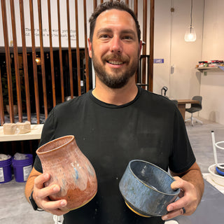 A member holding a rounded peach vase with white and blue drips beside a mottled blue bowl at The Clay Hole pottery studio in Draper, Utah