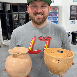 A member holding a round peach vase with a ruffled rim and a peach bowl with cutout holes and handles at The Clay Hole pottery studio in Draper, Utah