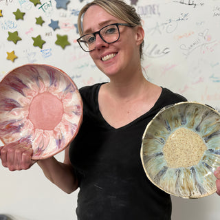 A member holding two bowls with streaks radiating outward, one pink and white and one blue-green with a tan center at The Clay Hole pottery studio in Draper, Utah