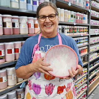 A member in an apron holding a wide bowl with soft pink and white streaks and a pink rim at The Clay Hole pottery studio in Draper, Utah