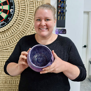 A member holding a purple bowl with white speckled glaze, a spiral in the bottom and a small spout at The Clay Hole pottery studio in Draper, Utah