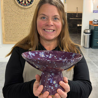A member holding a footed bowl with a deep purple glaze covered in pale blue and white speckles at The Clay Hole pottery studio in Draper, Utah
