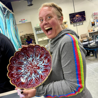 A member holding a scalloped edge bowl with deep red glaze, a pale blue starburst pattern and a gold rim at The Clay Hole pottery studio in Draper, Utah