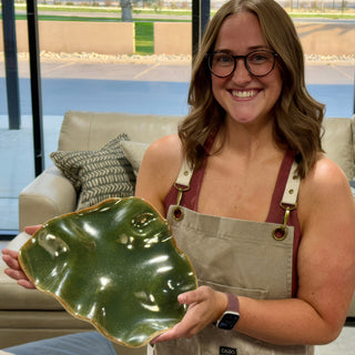 A member holding a rippled olive green dish with a glossy glaze and a gold colored edge at The Clay Hole pottery studio in Draper, Utah