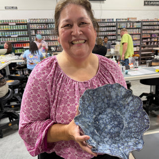 A member holding a wide ruffled bowl with a mottled blue and white glaze at The Clay Hole pottery studio in Draper, Utah