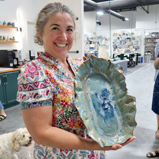 A member holding a long oval platter with a ruffled edge and blue, teal and white glaze at The Clay Hole pottery studio in Draper, Utah