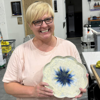 A member holding a scalloped edge plate in pearly white glaze with a deep blue starburst in the center at The Clay Hole pottery studio in Draper, Utah