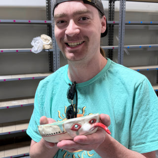 A member holding a small white dish shaped like a creature with red rimmed eyes and a curled red tongue at The Clay Hole pottery studio in Draper, Utah