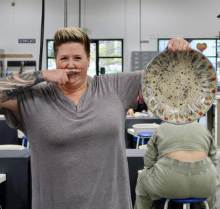 A member holding up a large round plate with a speckled cream center and a colorful petal patterned rim at The Clay Hole pottery studio in Draper, Utah