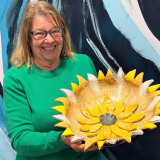 A member holding a large bowl shaped like a sunflower with bright yellow petals and a gray center at The Clay Hole pottery studio in Draper, Utah