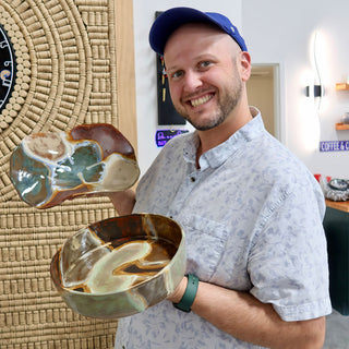 A member holding a wavy-edged dish and a deep bowl, both with swirled brown, cream and green glaze at The Clay Hole pottery studio in Draper, Utah