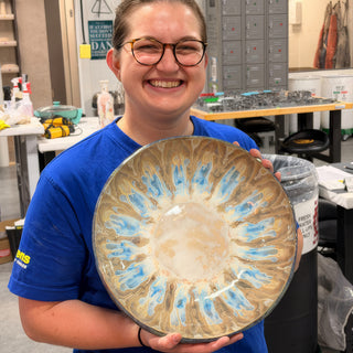A member holding a large round plate in tan and cream glaze with blue streaks spreading out from the center at The Clay Hole pottery studio in Draper, Utah