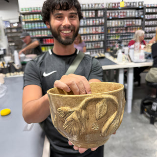 A member holding a tan speckled bowl with raised flowers and leaves around the side at The Clay Hole pottery studio in Draper, Utah