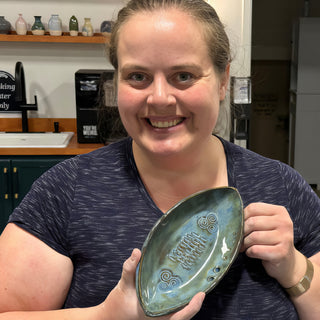 A member holding a pointed oval teal dish with spiral designs, a wavy line pattern and small holes at The Clay Hole pottery studio in Draper, Utah